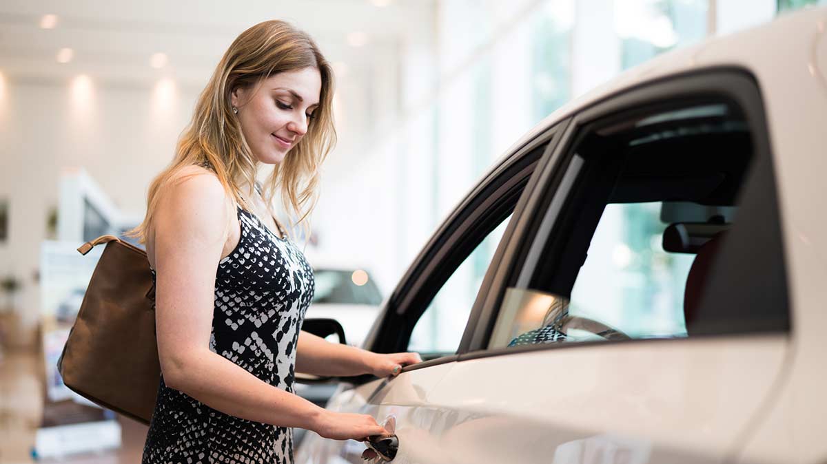 Woman is in a dealership buying a new car - opening a floor model car door.