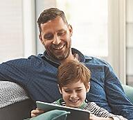 Father and son sitting in the couch, watching tablet together.