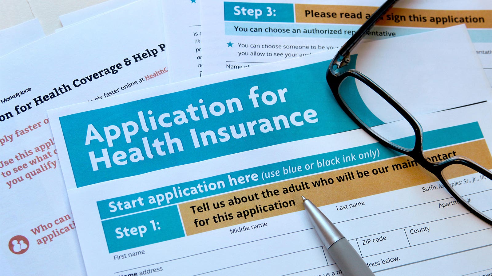 Glasses and a pen lay atop several insurance application forms.