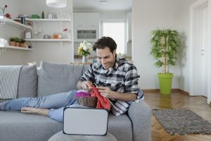 A man knits in front of his tablet while volunteering virtually