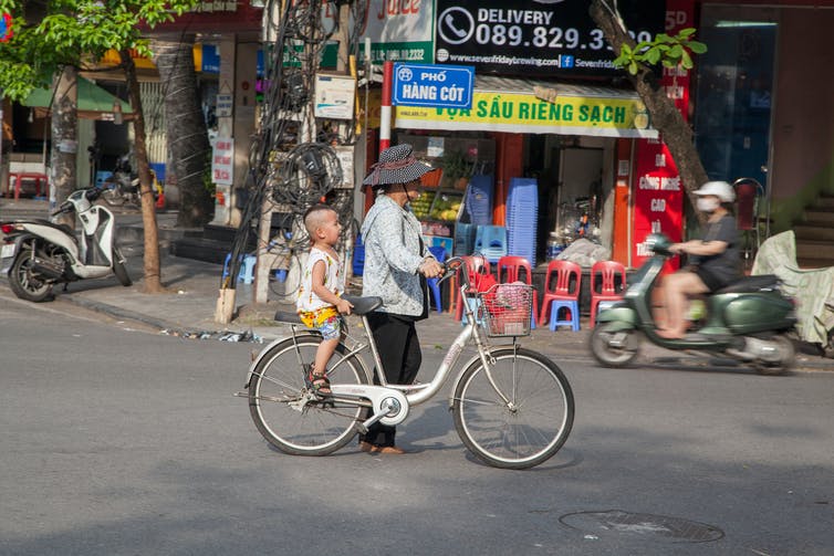 A woman pushes a bike with a small child down a city street.