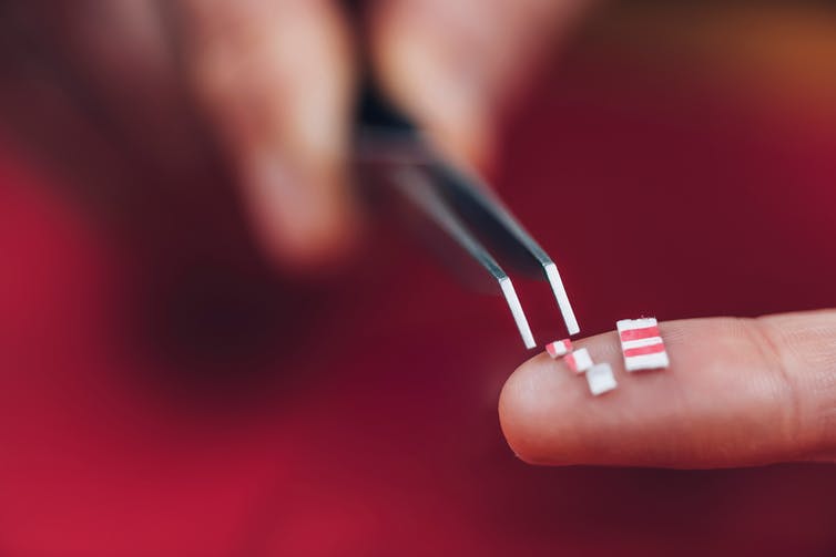 close-up of a hand holding tweezers handling small squares of cardboard that are microdose tabs