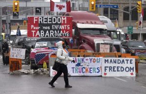 A woman crosses the street in front of vehicles parked as part of the trucker protest, Tuesday, Feb. 8, 2022 in Ottawa. THE CANADIAN PRESS/Adrian Wyld