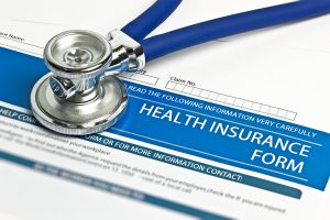 A stethoscope rests on top of a sheet of health insurance paperwork.