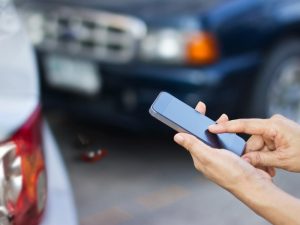 In the right corner, a woman's hand is extended into the frame. She is holding a smart phone. in front of a traffic accident.