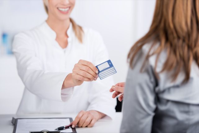 Smiling young doctor giving health card to a patient