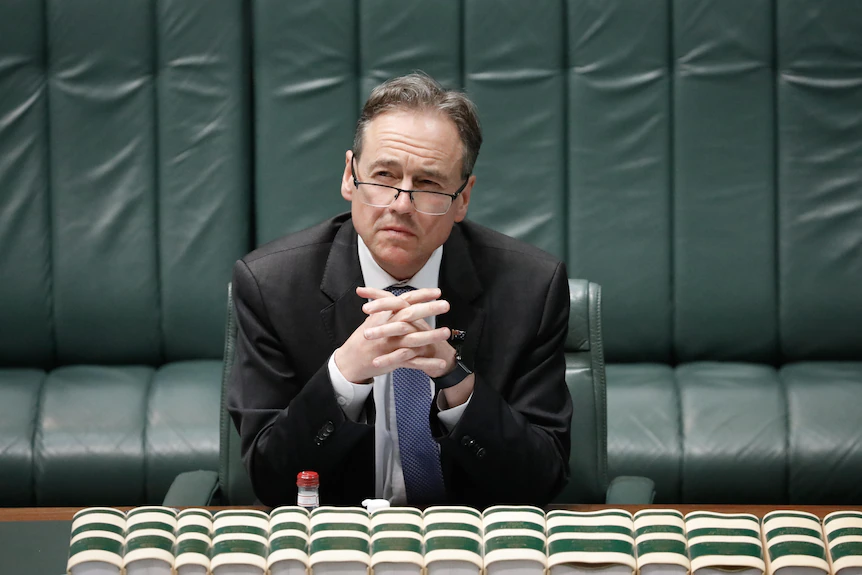 Hunt sitting looking upwards over glasses with fingers interlocked.