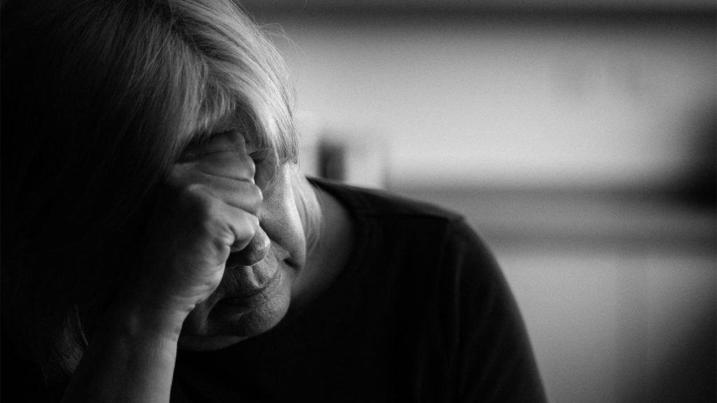 A portrait of a senior woman with head on her hand alone at home.