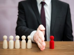 A man in a suit uses his hand to segregate a single red wooden block from a group of five other blocks.