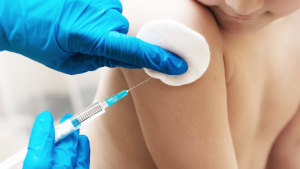 A close-up image of a child receiving a shot in the arm from a gloved doctor.