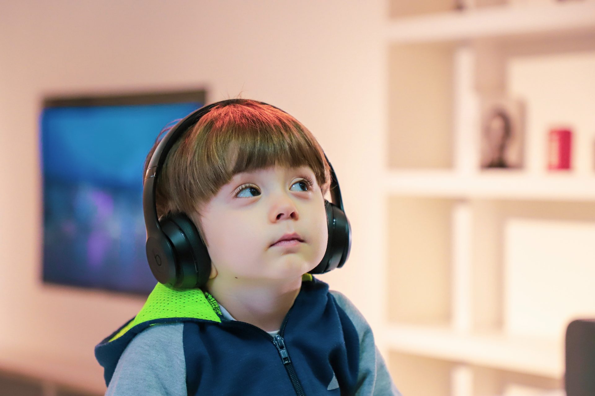 A young boy wearing a blue jacket sits with headphones over his ears.