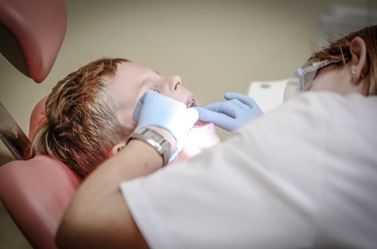 A child in a dentist's chair, obscured by the dentist's shoulder and hands.