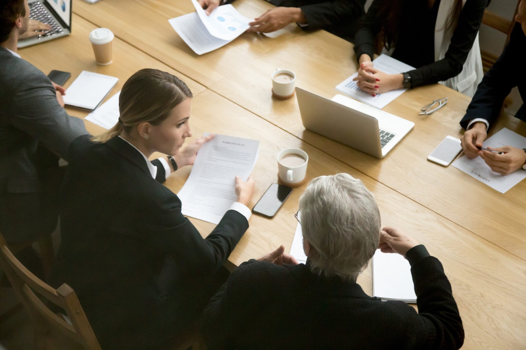 Negotiations concept, different businesspeople discussing deal details at group meeting, young and senior partners team thinking talking consulting about contract sitting at conference office table