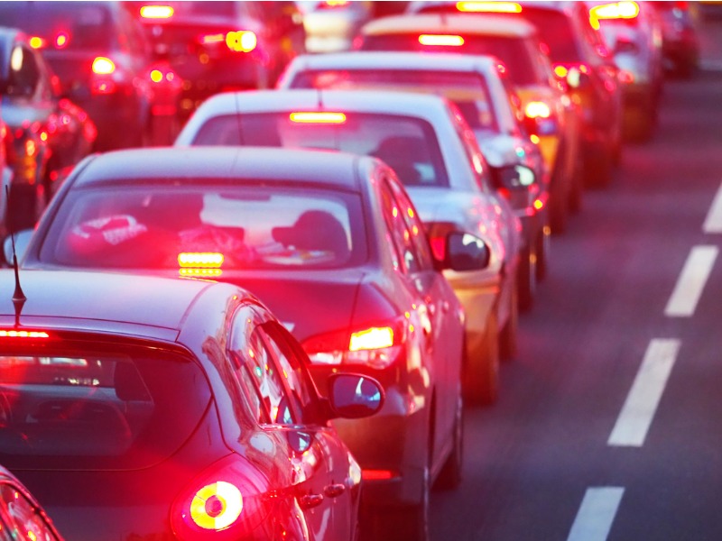 A row of cars in the evening on a busy road, their brake lights are on.