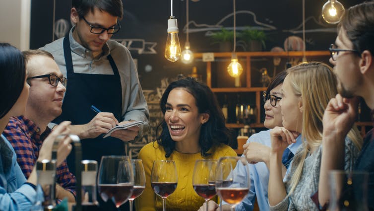 Friends sitting around restaurant table, waiter taking orders