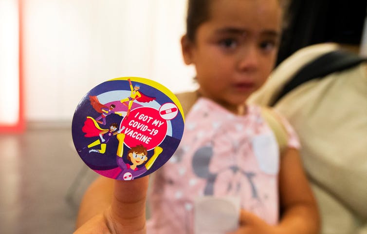 young girl shows off her 'I got my COVID-19 vaccine' sticker