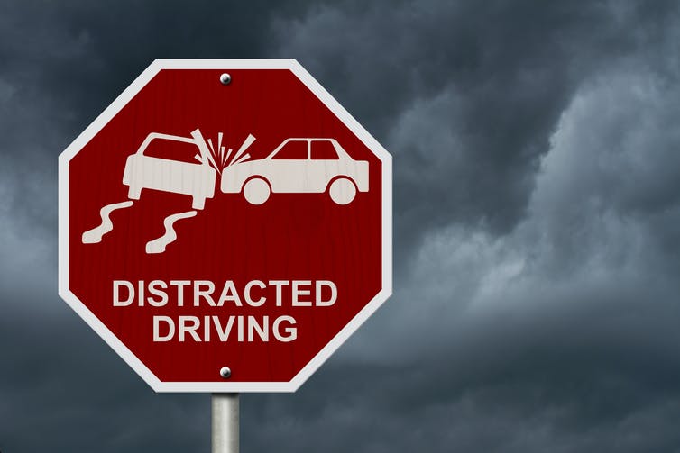 a red road sign showing a graphic of a car crash with the words DISTRACTED DRIVING