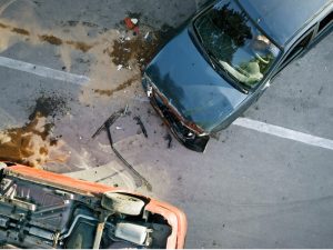 elevated view of two cars in an accident. Bottom left car is flipped over, while the top right car is damaged badly in the front hood.