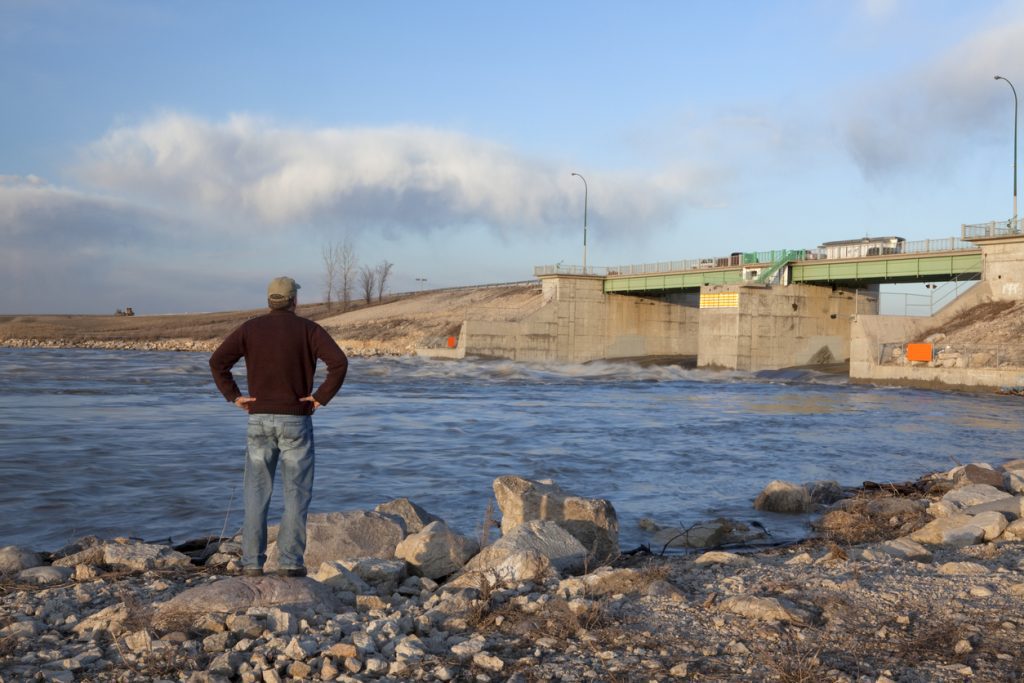 Image of man standing with his hands on his hips, looking at Winnipeg's red river floodway