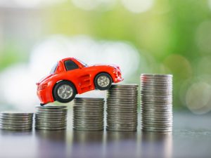 A red toy car rests on top of columns of stacked coins, each coin increasing in size.