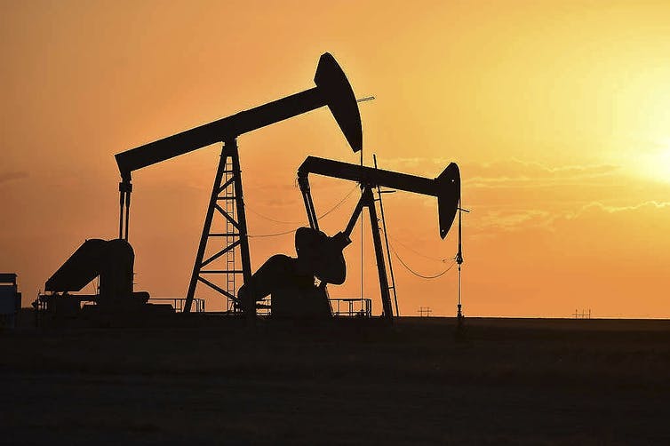 Two oil pumps silhouetted against the sky as the sun sets