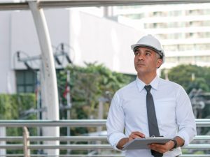 A man in a white button down shirt with a dark tie is holding a clipboard outside.