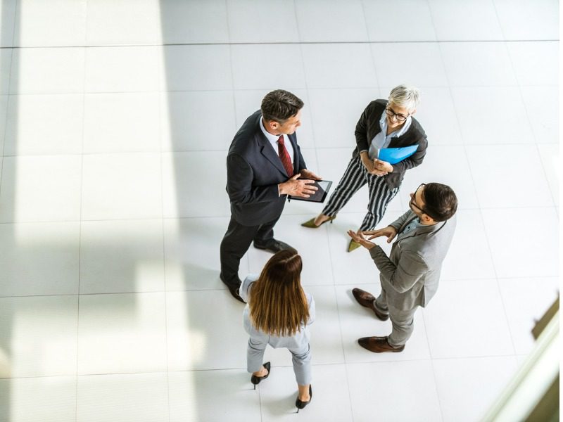 High angle photo of four business people standing in a group, gathered on a wide open office floor