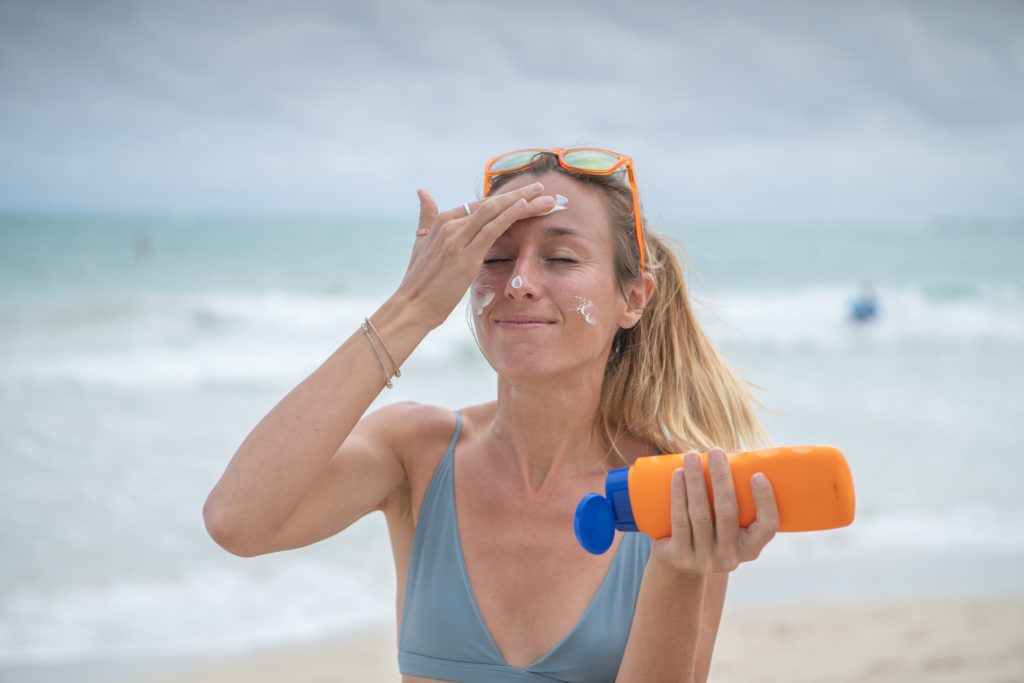 Summertime - Young woman on beach applying sunscreen on her face, protection on skin and sunbathing tan concept