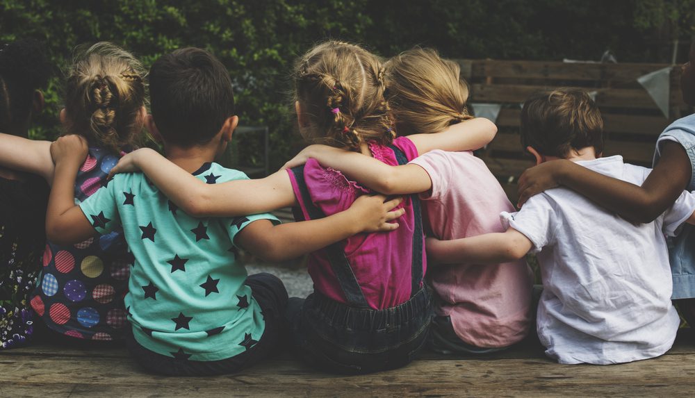 Group of kindergarteners sit with their backs to the camera and their arms around each other