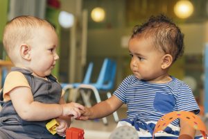 Two toddlers hold hands while playing together at daycare