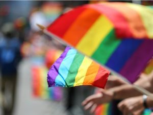 A row of Pride flags being waved by people standing amid a crowd