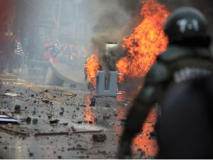 Riot police dealing with a protest and fire on a city street.