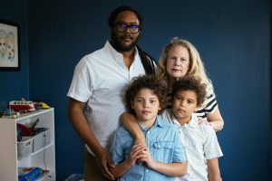 A family stands together in a room painted dark blue.