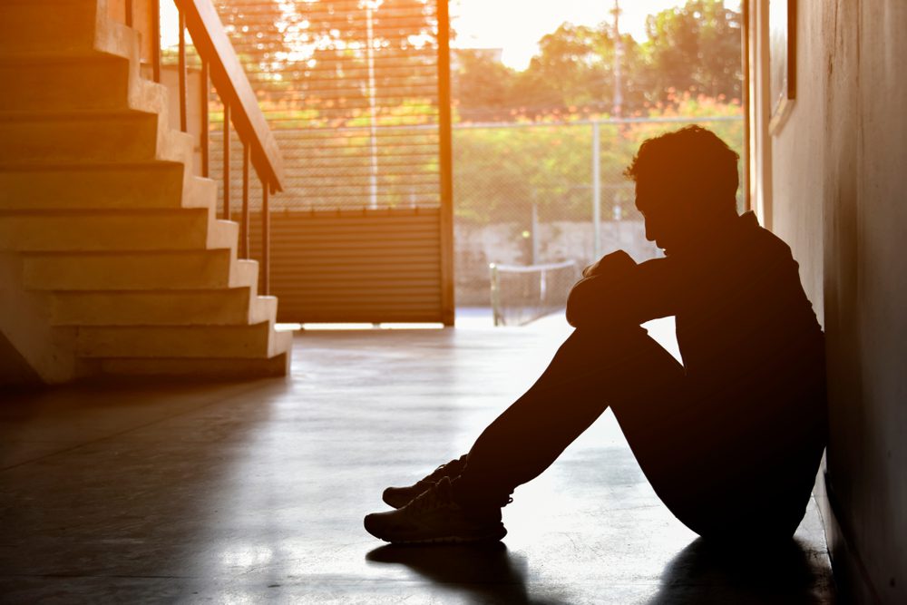 Man sits on the floor, back against the wall, with his hands on his knees