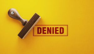 Wooden denied stamp on yellow background. Horizontal composition with copy space.