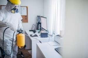 One man in protective suit disinfecting office work space