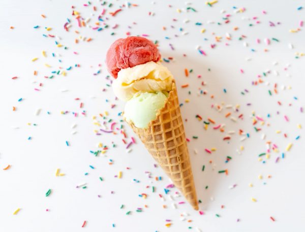 Ice cream cone filled with three types of ice cream and sprinkles on white table
