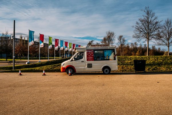 Ice cream van parked near a park with flags in the background