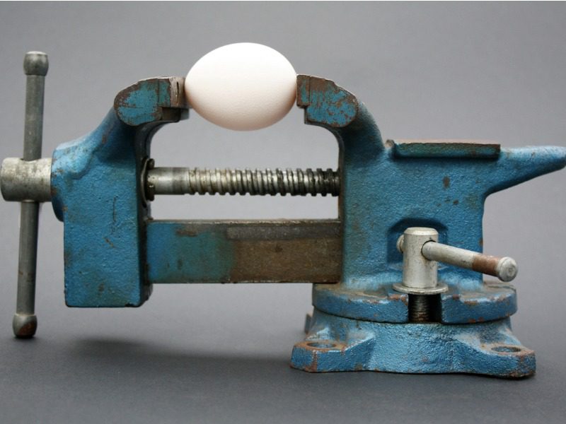 Egg in a vice to illustrate high pressure on workers.