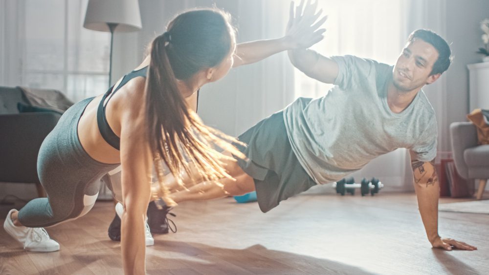 Athletic Couple in Workout Clothes Doing Push Up Exercises and Giving Each Other a High Five in Their Bright and Spacious Living Room