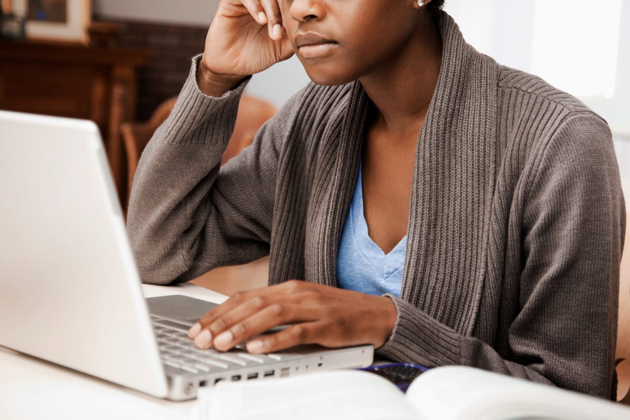 A photo shows a woman using a laptop with a notepad on the desk beside it.