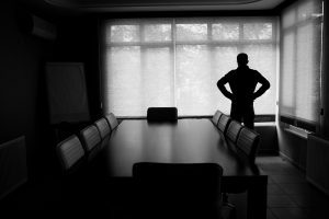 Silhouette Of Lonely Businessman Standing By Boardroom Table In Office.The chairs around table are empty.He looks desperate.The black and white color and dark atmosphere is used for economic depression feel.