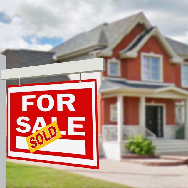 A red two-story house with a for sale sign in front