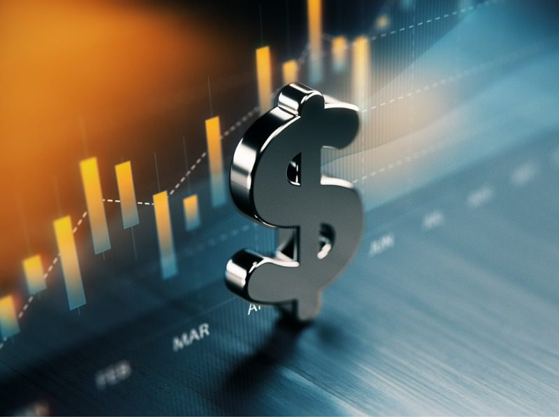 American dollar symbol standing on wood surface in front of a graph.