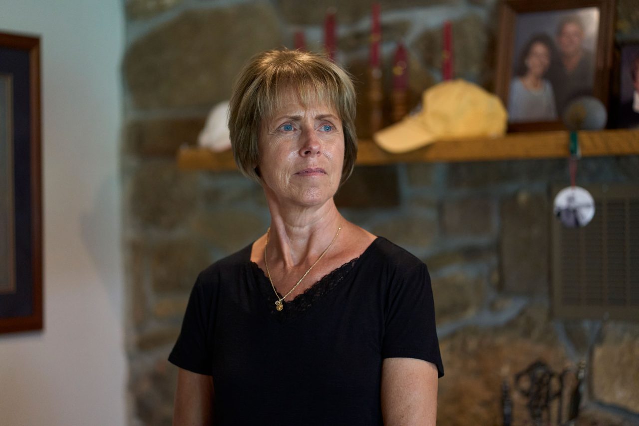 A woman in a black shirt stands in front of a mantlepiece.