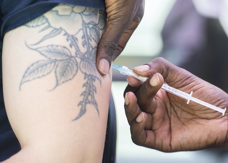 An arm with a tattoo of a flower and leaves being injected with a syringe