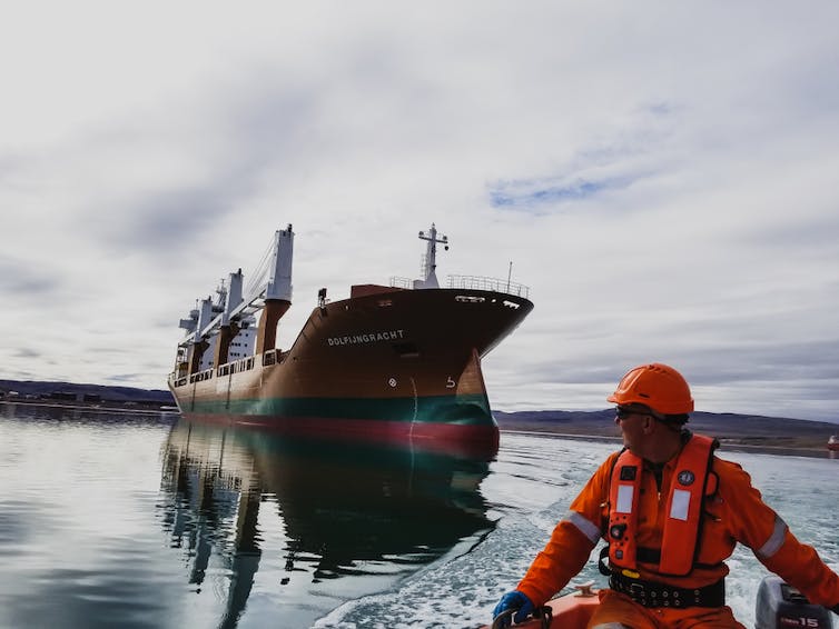 Un gros navire est accompagné dans l’eau par un homme en tenue orange