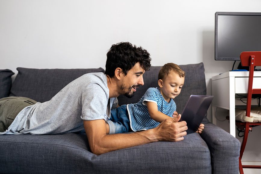 Dad playing with son on the couch watching the tablet