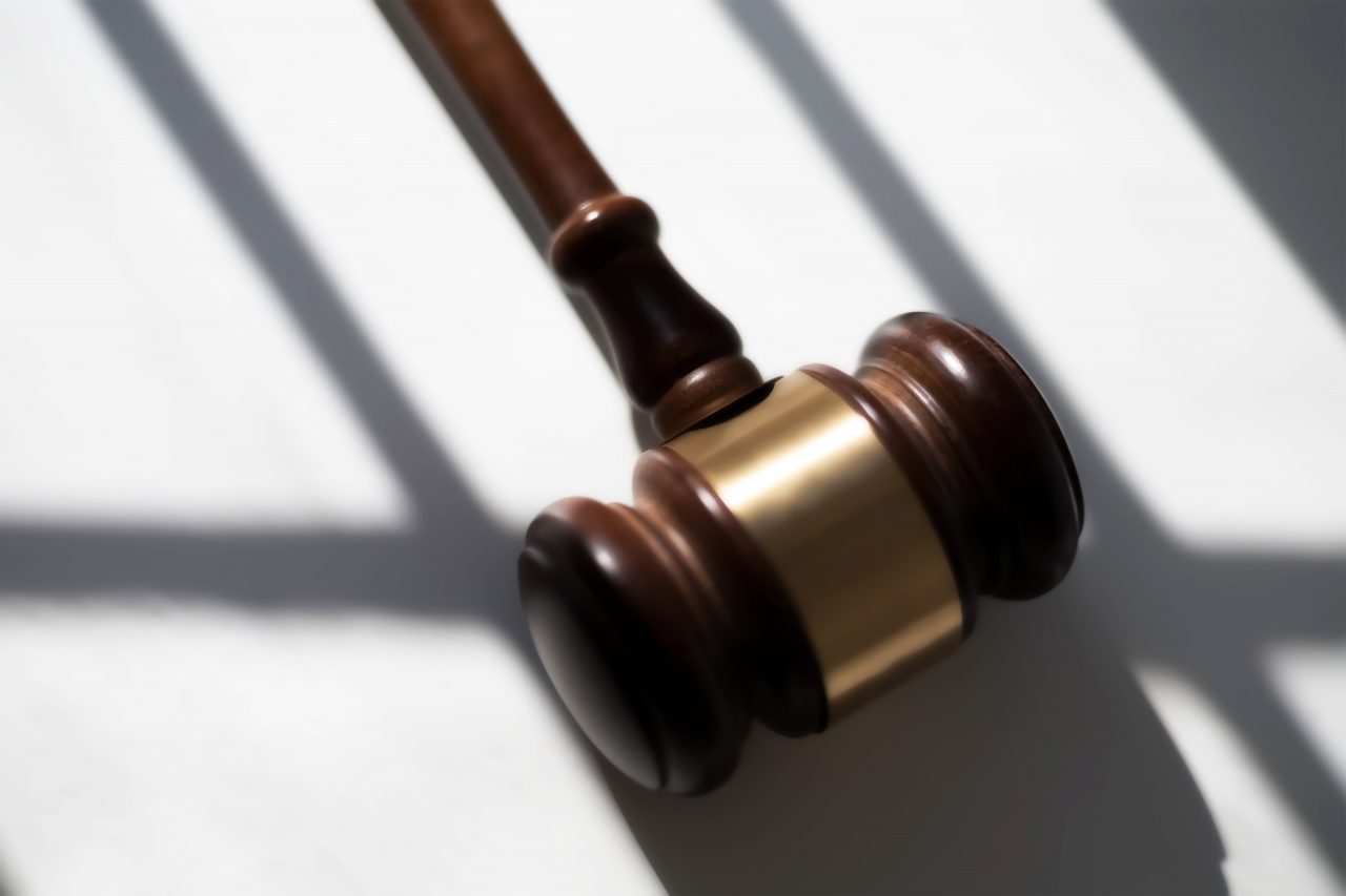 A photo shows a judge's gavel resting on a surface surrounded by shadows.