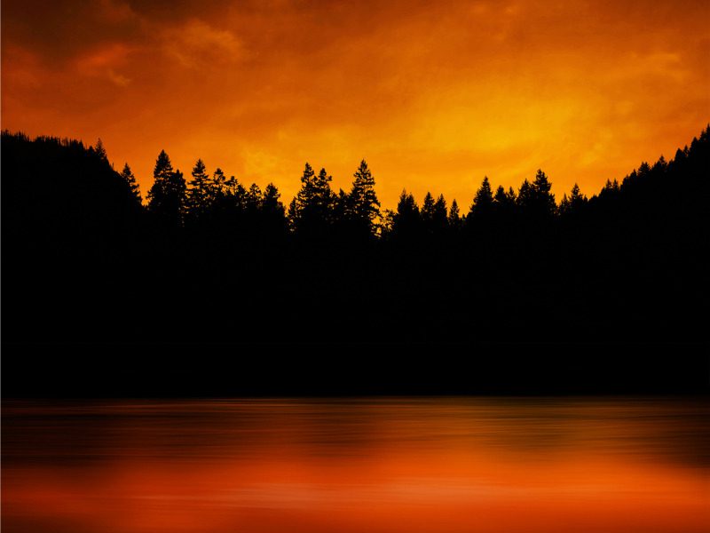 Forest fire with trees in silhouette and reflection in lake